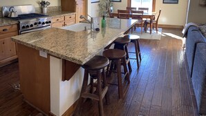 A kitchen with wooden cabinets, a granite countertop, a stove, and a dining area with wooden chairs and a table.
