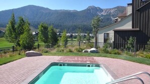 A swimming pool with a mountain view, surrounded by a fenced yard with trees and rocks.