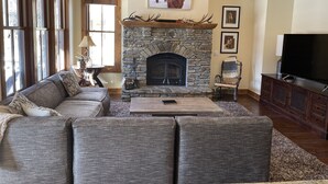A living room with a stone fireplace, a sofa, a television, and a ceiling fan.