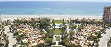 A resort with multiple buildings, a central pool area, and a beach in the background.