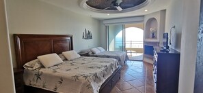 Ein Hotelzimmer mit zwei Betten, einem Deckenventilator, einem Balkon mit Blick und einem Schreibtisch mit Computer.