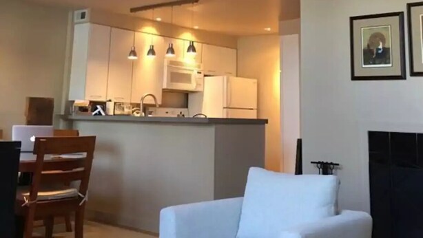 Un soggiorno moderno con un divano bianco, un tavolo da pranzo in legno e sedie. Si nota anche un angolo cottura con mobili bianchi e un forno a microonde.