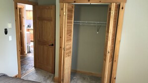 Una habitación con cama, un armario de madera con barra para colgar ropa y una puerta abierta que da a una cocina.