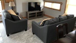 Una sala de estar con dos sofás grises, un mueble de entretenimiento de madera, un televisor de pantalla plana y una lámpara.