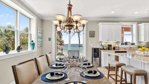 A dining area with a wooden table set for six, a chandelier, and a view of the ocean. - Ocean Sands 4BR Beachfront Home in Indian Rocks (Indian Rocks Beach)