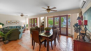 A spacious living room with a dining area, ceiling fans, and large windows offering a view of the outdoors. - Beachfront, Private Pool, Pure Luxury at  Bahia Pez Vela, Villa Las Olas #4 (Playa Ocotal)