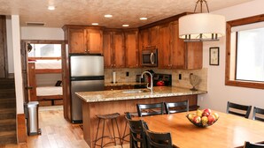 A kitchen with wooden cabinets, a stainless steel refrigerator, a microwave, and a granite countertop. There is a dining table with chairs and a fruit bowl. - 4 BR/4 BA Townhome - Spacious, comfortable, the perfect getaway! (Park City)