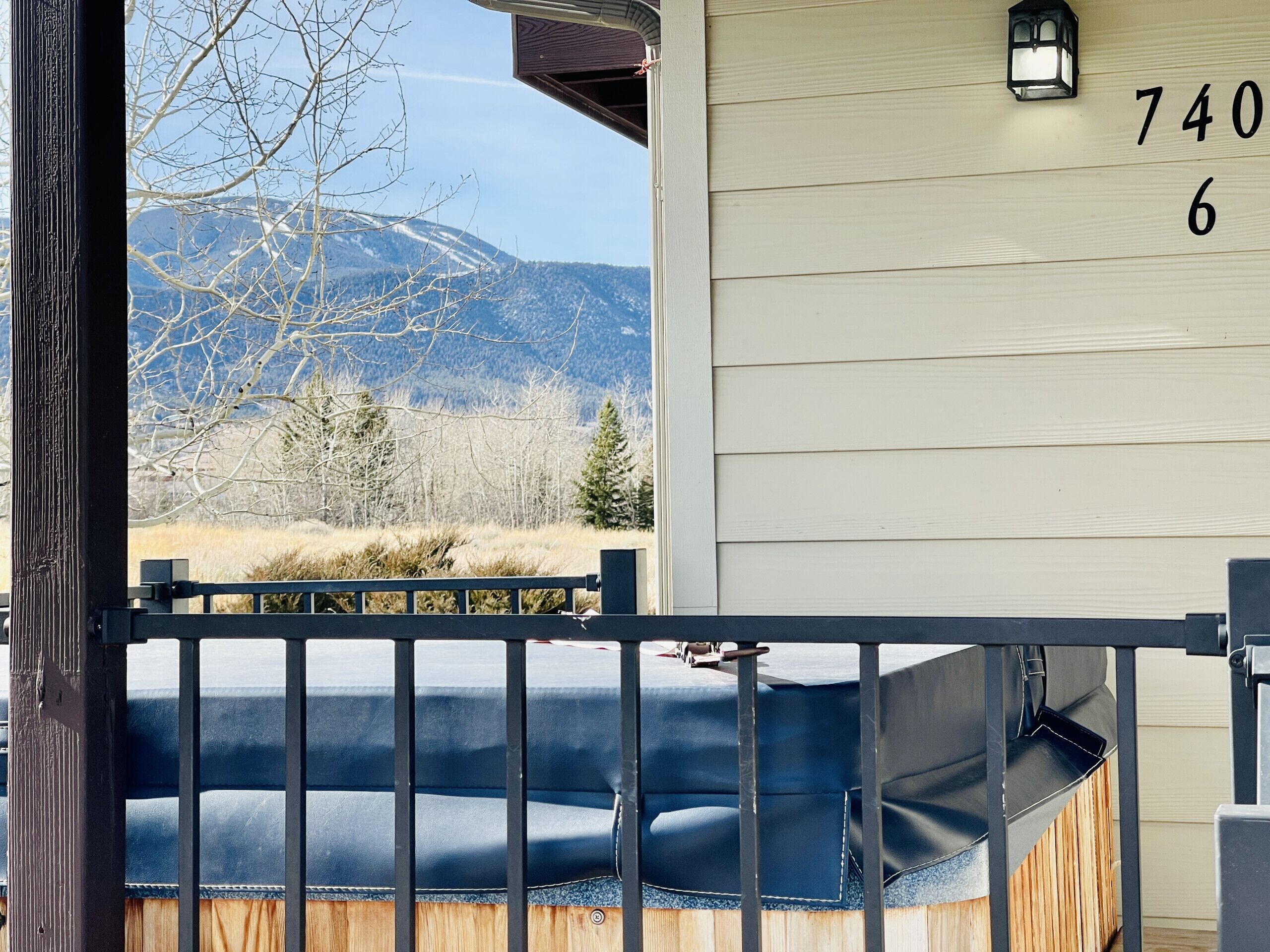 A wooden house with a number '740' on the wall, a black metal gate, and a view of mountains and trees.