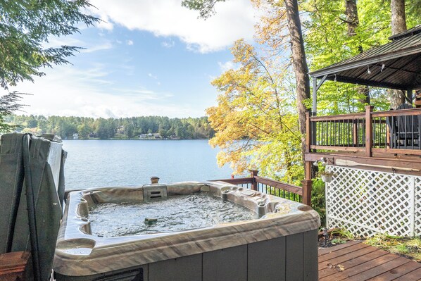 A hot tub on a wooden deck with a view of a lake and trees.