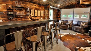 A rustic bar area with wooden bar stools, a cowhide rug, and leather furniture in a cozy, cabin-like interior. - Lakeside Retreat- Family and Pet Friendly  (Fort Ann)