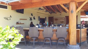 Un espace bar extérieur avec des chaises en osier, un plafond en bois et un sol en pierre.