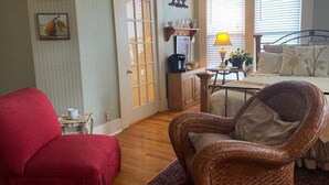 Een gezellige woonkamer met een rode bank, een rieten fauteuil en een eethoek met een tafel en stoelen.
