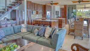 A modern kitchen with wooden cabinets, a central island, and a dining area with wicker chairs.