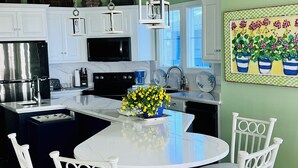 A modern kitchen with white cabinetry, a central island with a blue countertop, and a dining area with white chairs. - Oceanfront & Soundfront! Luxury Beachfront, Pool, Private Exclusive West End   (Ocean Isle Beach)