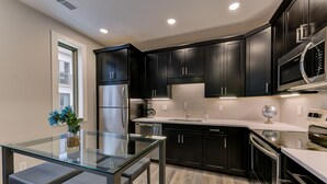 Una cocina moderna con armarios oscuros, electrodomésticos de acero inoxidable y una mesa de comedor de vidrio.