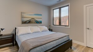 Un dormitorio con cama, mesita de noche, escritorio, ventana y puerta.