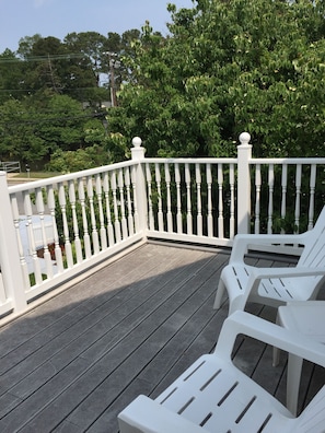 A wooden deck with white railings and two white plastic chairs.