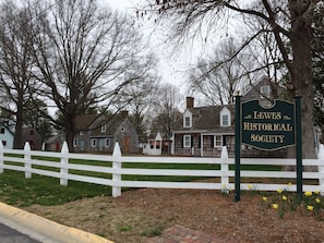 A sign for the Lewes Historical Society with a white picket fence and houses in the background.