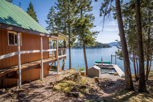 Une cabane dotée d’une terrasse donnant sur un lac, entourée d’arbres.