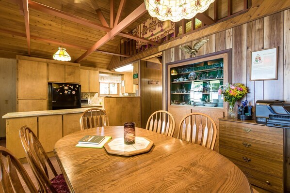 A wooden interior with a dining table, chairs, a refrigerator, and a bar area with shelves. - Grandma's cabin in the woods on the lake! (Rollins)