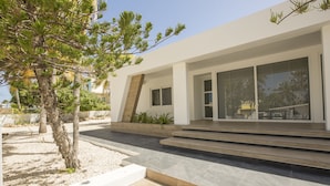 Un edificio moderno con grandes ventanales, una terraza de madera y un jardín ajardinado con un árbol.