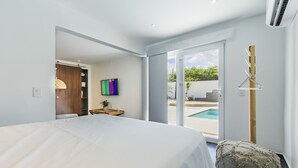 Un dormitorio moderno con una cama grande, una mesita de noche de madera, un cuadro abstracto colorido y vistas a una piscina a través de una puerta corrediza de vidrio.