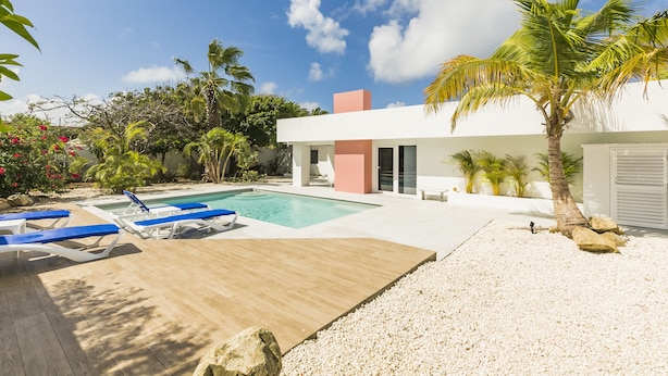 Una casa moderna con piscina, palmeras y una terraza de madera.