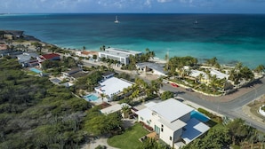 Vista aérea de una zona residencial costera con casas, una piscina y una carretera que lleva a la playa.