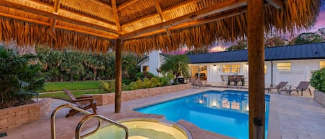 Piscina com hidromassagem, cercada por espreguiçadeiras e um espaço coberto com varanda.