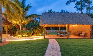 A thatched-roof outdoor area with a paved walkway, seating, and string lights.