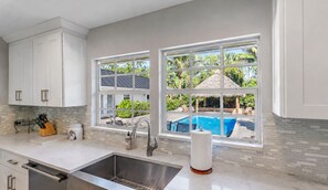 Una cocina con vista a una piscina, un lavamanos y una ventana con vista a la vegetación.