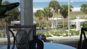 A view from a window overlooking a beach with palm trees, a white gazebo, and a road with cars. - Stunning Sunset Views-Steps to Siesta Key Beach-A Couples' Romantic Beach Condo (Siesta Key)