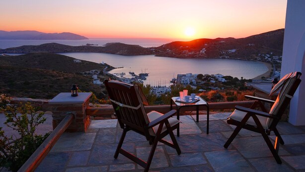 Eine Terrasse mit zwei Stühlen und einem Tisch mit Blick auf die Küste bei Sonnenuntergang.