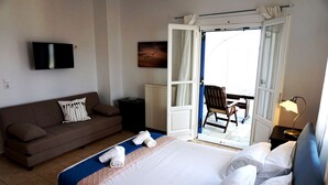 Ein Hotelzimmer mit Bett, Sofa, Fernseher, einem Gemälde und einer offenen Tür zum Balkon.