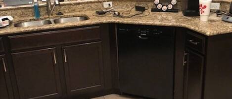 A kitchen with dark cabinets, a granite countertop, a dishwasher, and a coffee maker.