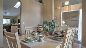 Ein Essbereich mit einem Tisch, gedeckt für vier Personen, umgeben von Stühlen. Auf dem Tisch steht ein Blumentopf, und der Raum verfügt über einen Deckenventilator und eine Kronleuchter.