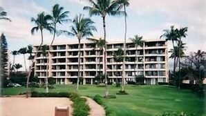 A multi-story hotel with a symmetrical facade, surrounded by palm trees and a well-maintained lawn. - Weekly and Monthly Discounts / Koa Lagoon Direct Oceanfront Top Floor Unit 603 (Kihei)