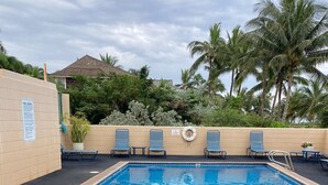A rectangular swimming pool with a tiled edge and a metal ladder. There are lounge chairs and a small table with a plant. A lifebuoy is attached to the wall. - Weekly and Monthly Discounts / Koa Lagoon Direct Oceanfront Top Floor Unit 603 (Kihei)