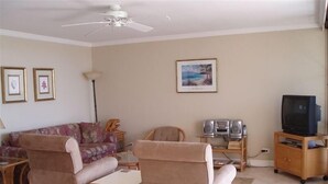 A living room with two sofas, a coffee table, a TV stand with a TV, speakers, and framed pictures on the wall. - Weekly and Monthly Discounts / Koa Lagoon Direct Oceanfront Top Floor Unit 603 (Kihei)