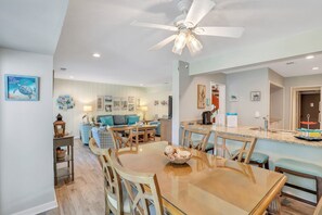 A spacious living area with a dining table, chairs, a ceiling fan, and a kitchen area with a sink and counter.