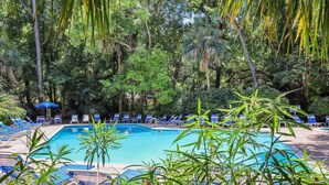 Una piscina circondata da vegetazione rigogliosa e comode poltrone blu.