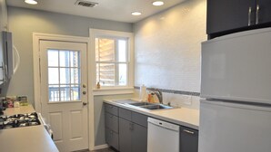 Una cocina compacta con un refrigerador blanco, un lavamanos y una ventana con persianas.