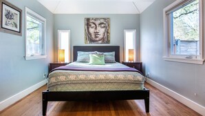 Un dormitorio con una cama centrada bajo un tragaluz, flanqueada por dos ventanas.