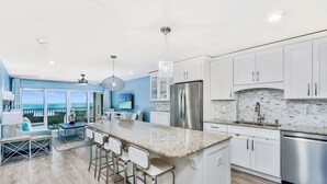 A modern kitchen with white cabinets, a granite countertop, stainless steel appliances, and a view to the outside. - On the Sand! Beachfront Pool & Views! Walk to Everything! (Fort Myers Beach)