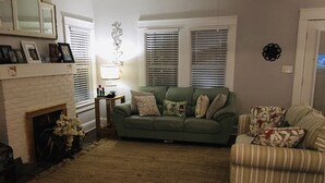 Ein Wohnzimmer mit einem grünen Sofa, einem gestreiften Sessel, einem Kamin und einem Teppich.
