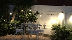 Eine Terrassengruppe im Freien mit Backsteinboden, weißen Metallstühlen und einer Lichterkette.