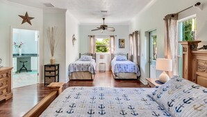 Une chambre à coucher décorée sur le thème de la marine, avec deux lits, un ventilateur de plafond et une vue sur l’extérieur.