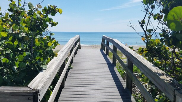 Une promenade en bois menant à une plage, avec un ciel dégagé.