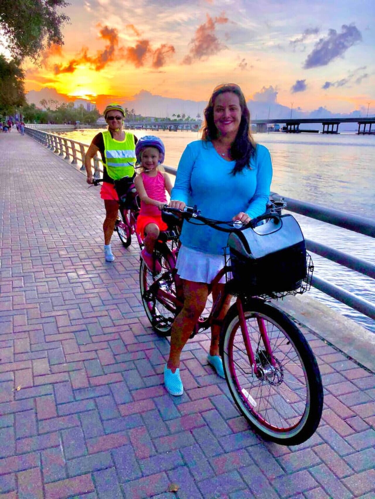 A paved walkway with a metal railing, a sunset in the background, and a body of water.