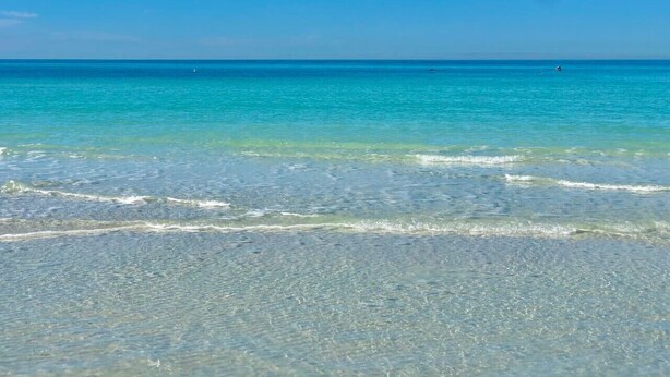 A beach with clear turquoise water and gentle waves.